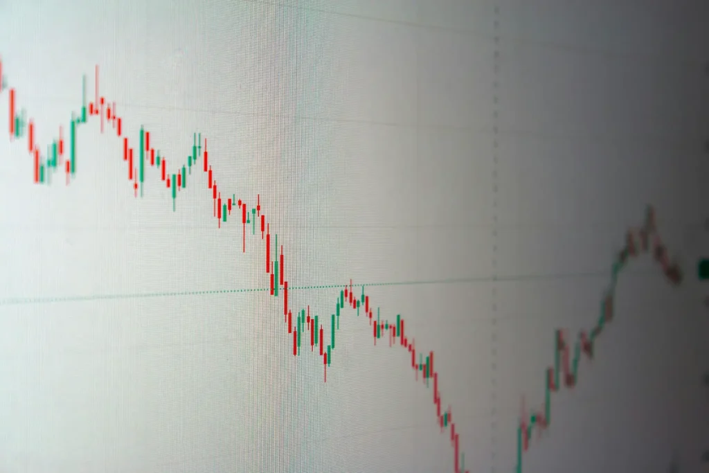 Gráfico de análise de investimentos em tela com linha de tendência em queda, barras verdes e vermelhas de candles e indicador horizontal no meio do painel, sugerindo volatilidade e movimento de baixa.